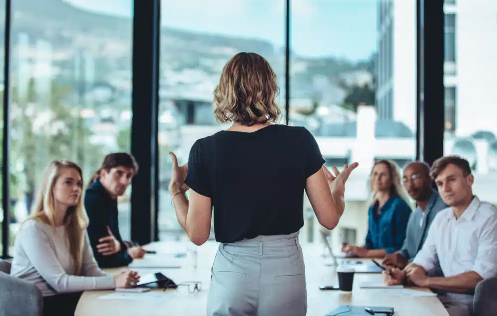 Leader standing at the end of the table speaking to colleagues.